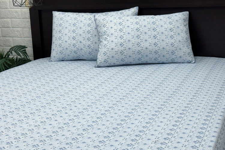A bed with a blue floral print bed sheet and two matching pillows.