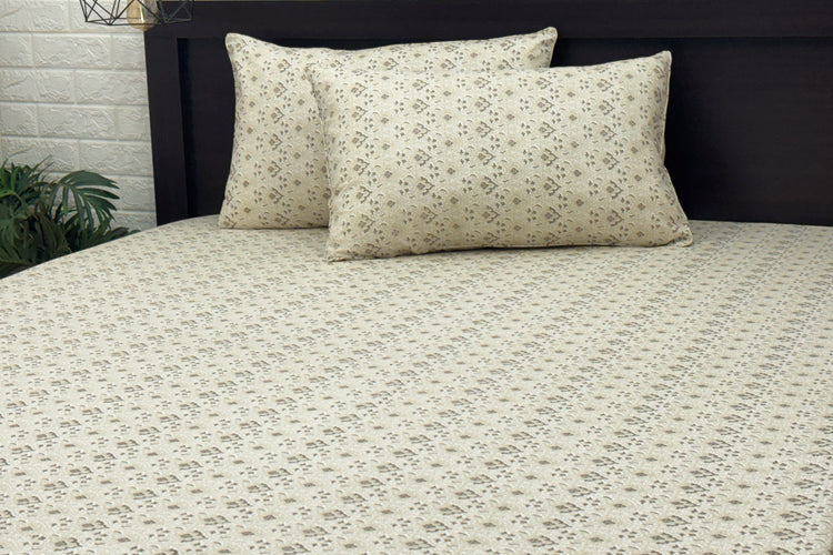 A neatly made bed with a beige floral-patterned sheet and two matching pillows .