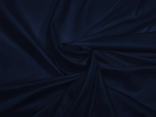 A smooth, dark navy blue fabric neatly folded into elegant, flowing drapery. The texture appears silky.