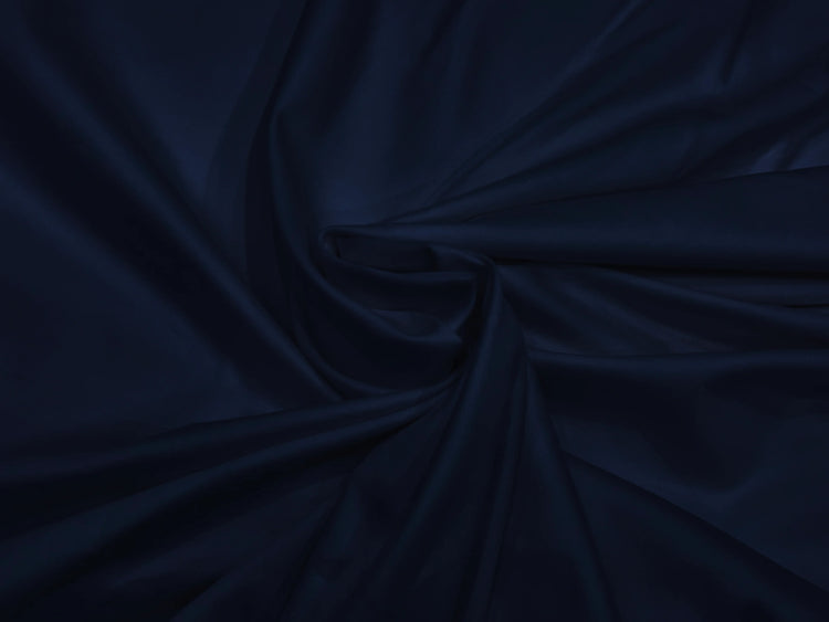 A smooth, dark navy blue fabric neatly folded into elegant, flowing drapery. The texture appears silky.