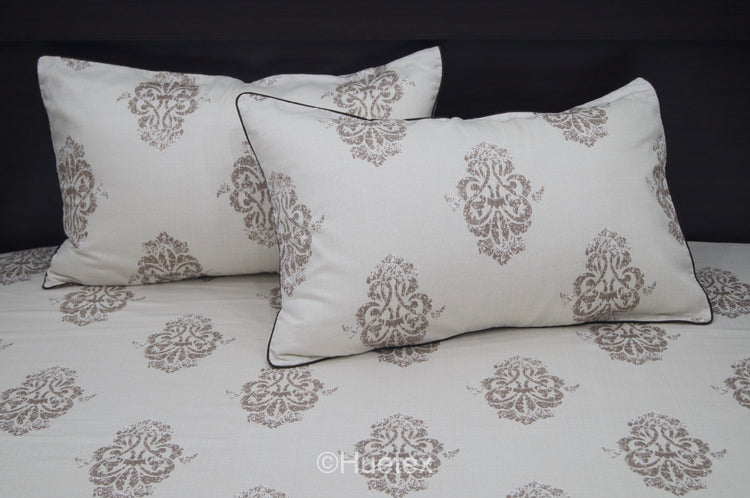 Bed with white and taupe ornate pattern, featuring two matching pillows 1.