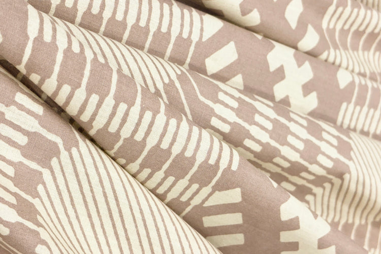 Close-up of folded fabric with geometric patterns in cream and taupe.