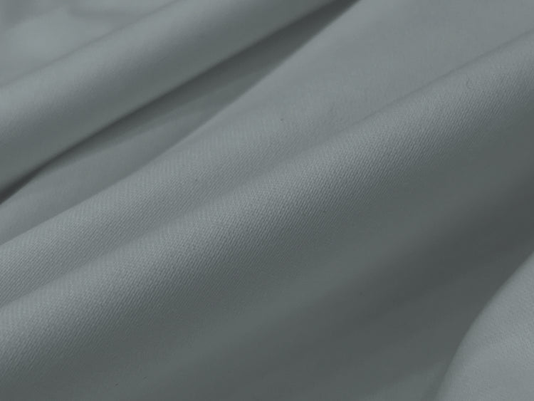 Close-up of smooth bedsheet, grayish fabric with soft folds creating a gentle wave pattern.