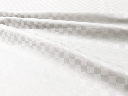 Close-up view of a white custom bed sheet with a sateen self square weave pattern 1.