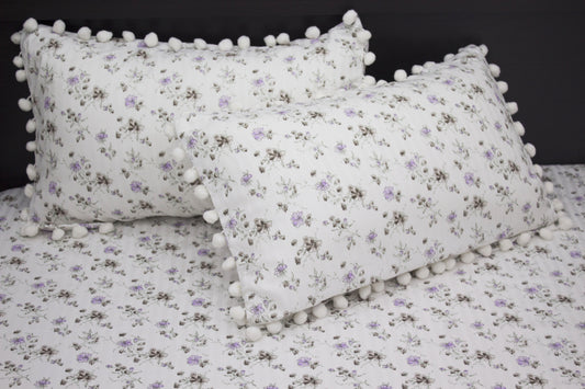 Two white pillows and bedsheet with a floral print and purple stripes on a bed.