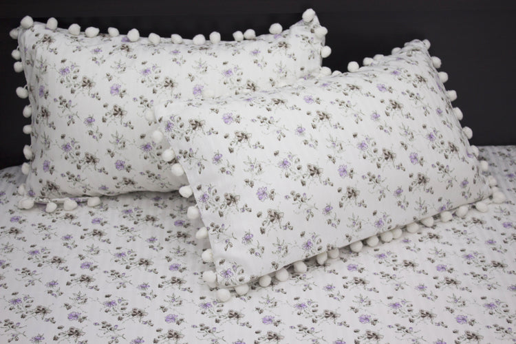 Two white pillows and bedsheet with a floral print and purple stripes on a bed.