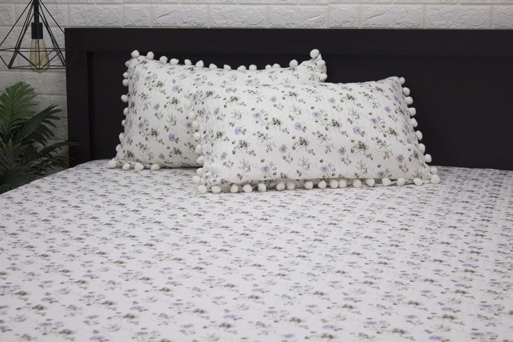 Two white pillows and bedsheet with a floral print and purple stripes on a bed 1.