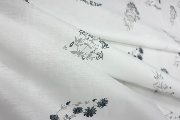 White fabric bedsheet with =floral patterns in grey and black.