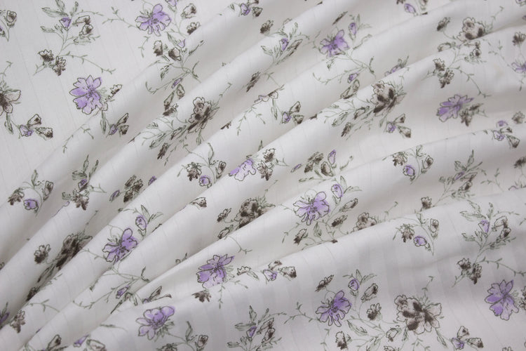 bedsheet with floral print and purple stripes on a bed with neatly folded.