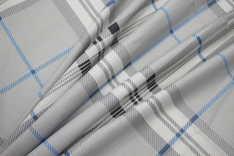 geometric pattern bedsheet on a bed, primarily in gray, blue, and white colors.