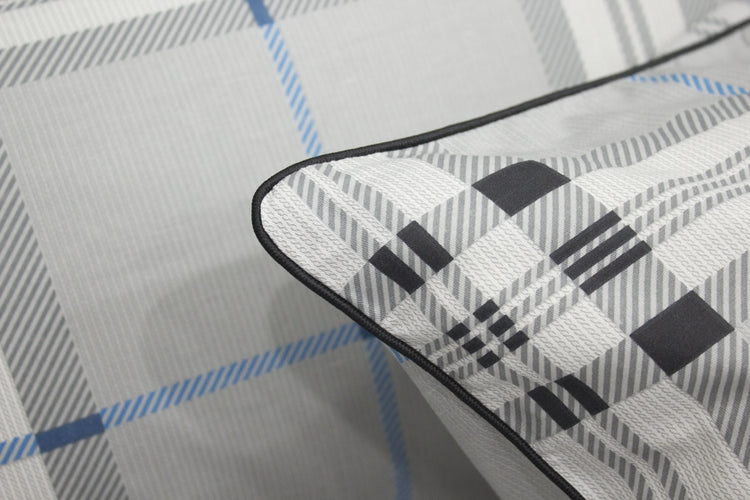 square pillow with a geometric pattern bedsheet on a bed, primarily in gray, blue, and white colors.