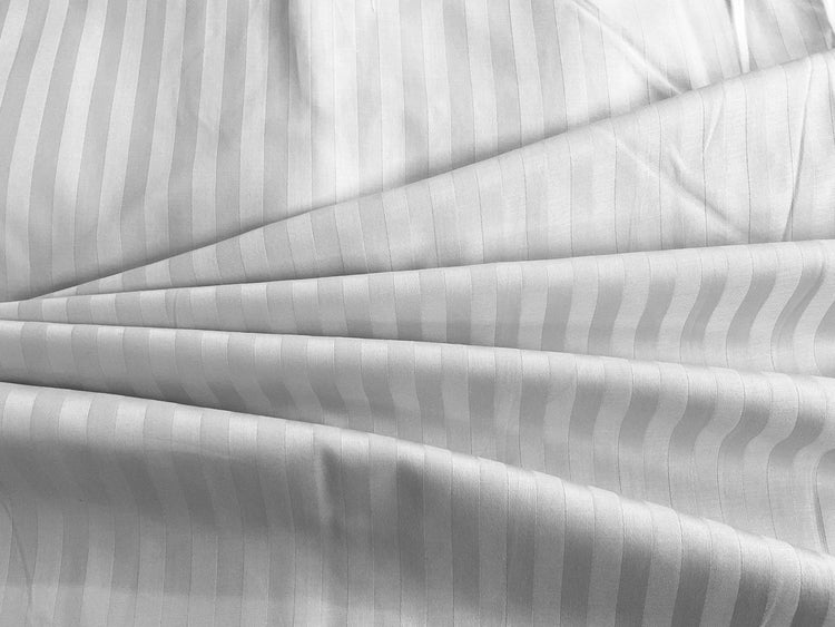 A close-up of a white sateen bed sheet with self stripes weave pattern.