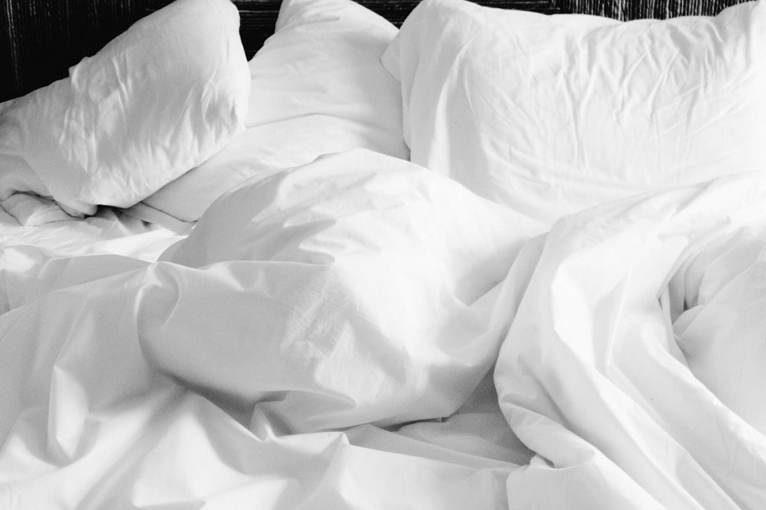 Unmade bed with crumpled white sheets and scattered pillows.