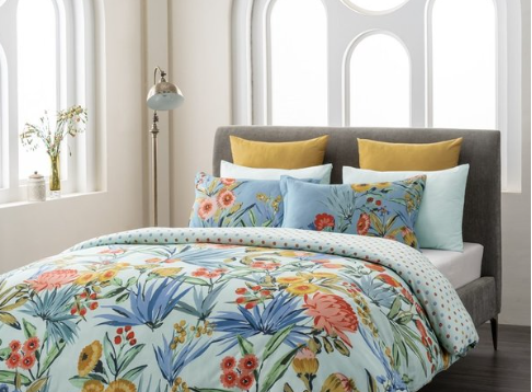 floral-patterned comforter featuring vibrant blue, yellow, and red flowers. Gray headboard, yellow accent pillows.