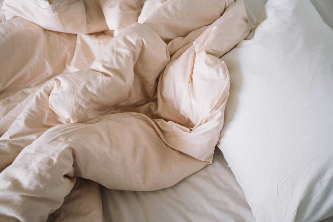 A cozy, unmade bed with crumpled, soft beige sheets and a white pillow, conveying a relaxed and inviting atmosphere, suggesting comfort and warmth.