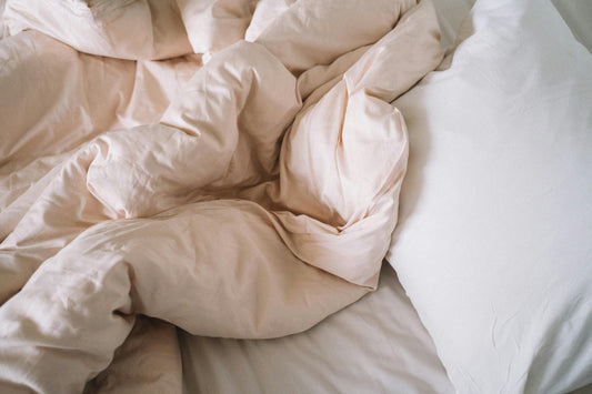 A cozy, unmade bed with crumpled, soft beige sheets and a white pillow, conveying a relaxed and inviting atmosphere, suggesting comfort and warmth.