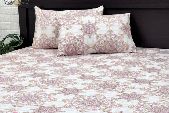 A bed dressed with a white and pink geometric-patterned bedsheet and matching pillows.