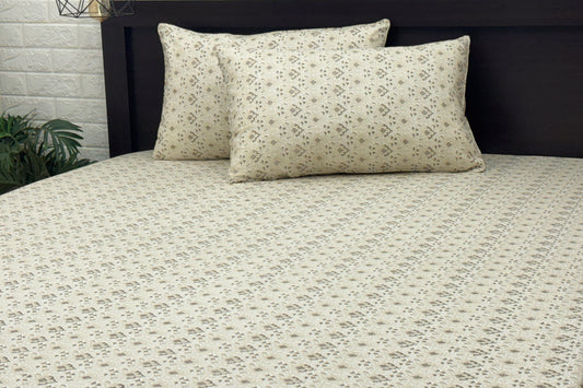 A neatly made bed with a beige floral-patterned sheet and two matching pillows .