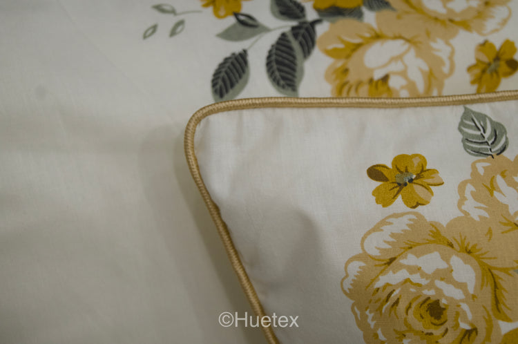 A neatly made bed with a cream sheet and  pillow, all featuring a pattern of yellow and green flowers 
