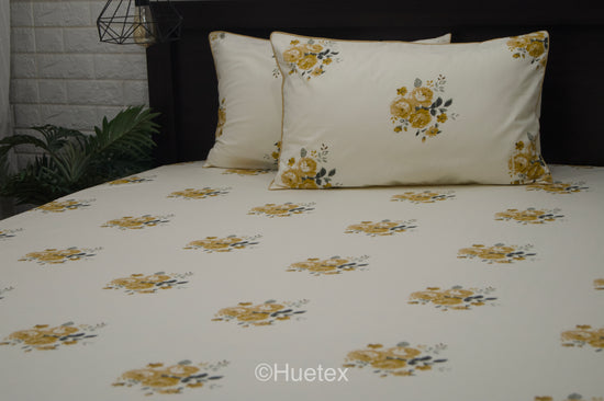 A neatly made bed with a cream sheet and two pillows, all featuring a pattern of yellow and green flowers 1.
