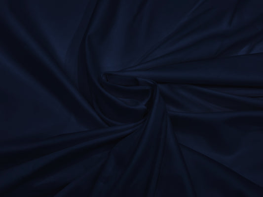 A smooth, dark navy blue fabric neatly folded into elegant, flowing drapery. The texture appears silky.