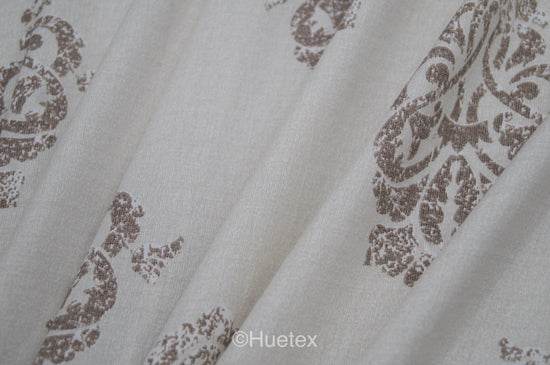 Bed with white and taupe ornate pattern .