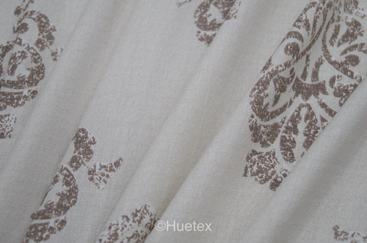 Bed with white and taupe ornate pattern .