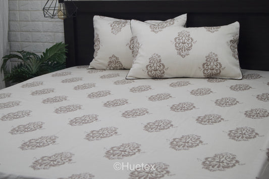 Bed with white and taupe ornate pattern, featuring two matching pillows.