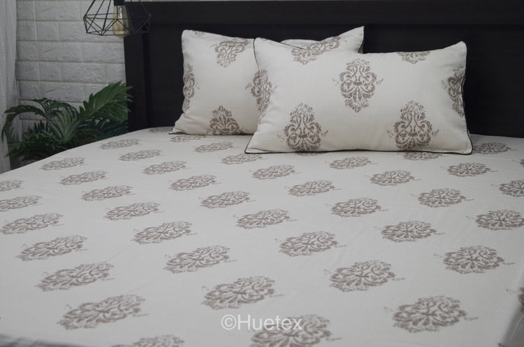 Bed with white and taupe ornate pattern, featuring two matching pillows.