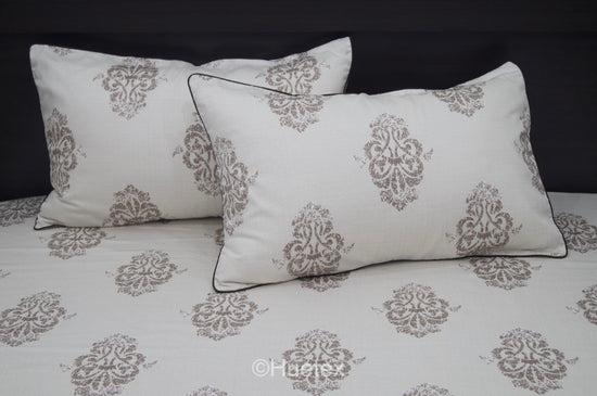 Bed with white and taupe ornate pattern, featuring two matching pillows 1.