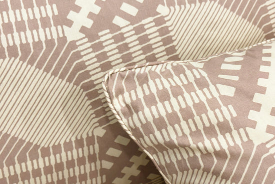 Close-up of a beige pillow with a geometric, circuit-like pattern in white