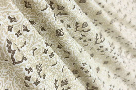 Close-up of beige fabric with intricate brown floral and paisley pattern bedsheet.