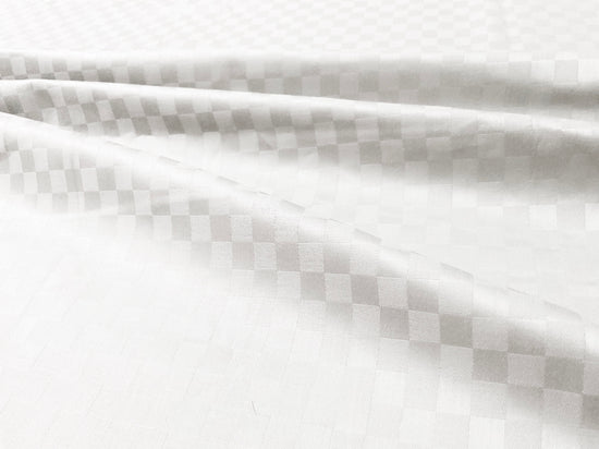 Close-up view of a white custom bed sheet with a sateen self square weave pattern 1.