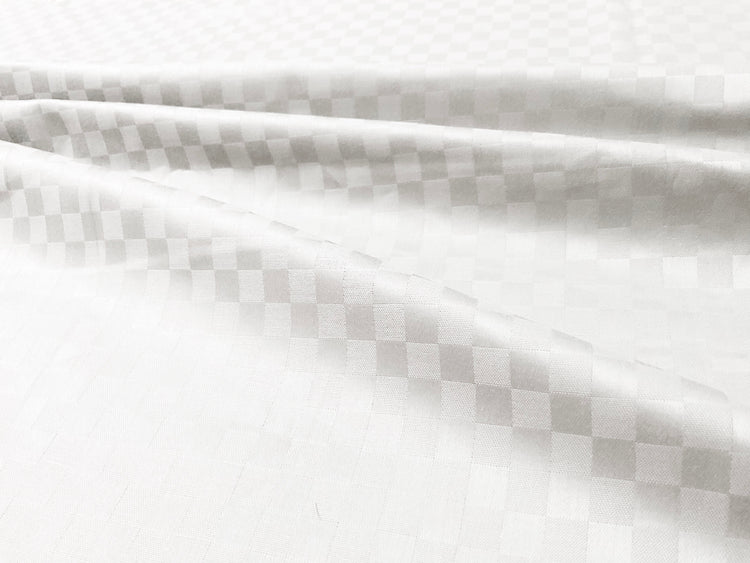 Close-up view of a white custom bed sheet with a sateen self square weave pattern 1.