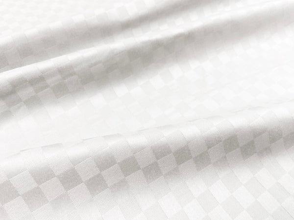 Close-up view of a white custom bed sheet with a sateen self square weave pattern 2.