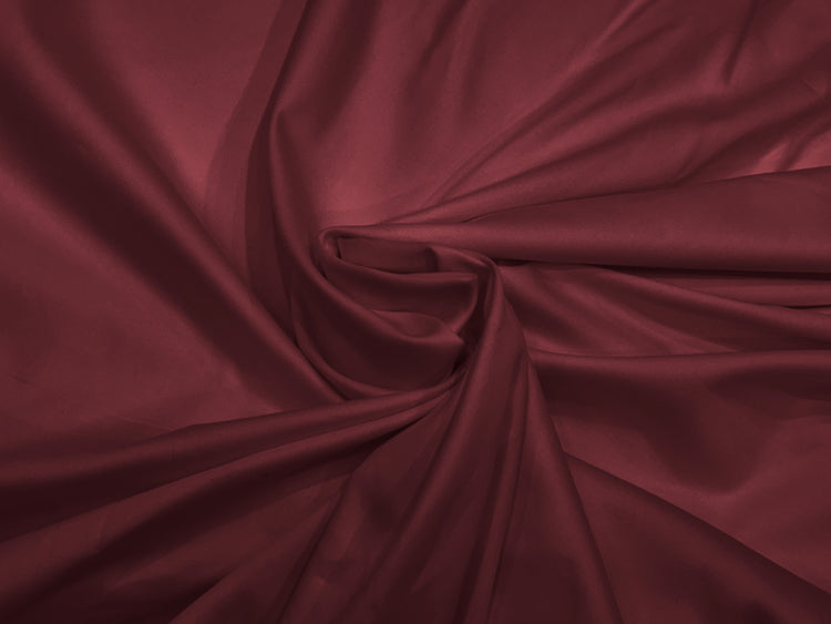 Deep red satin fabric bedsheet is draped and gathered in soft, swirling folds.