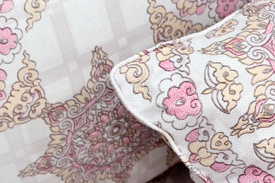 Ornate pillow with intricate floral patterns in pink, beige, and white tones
