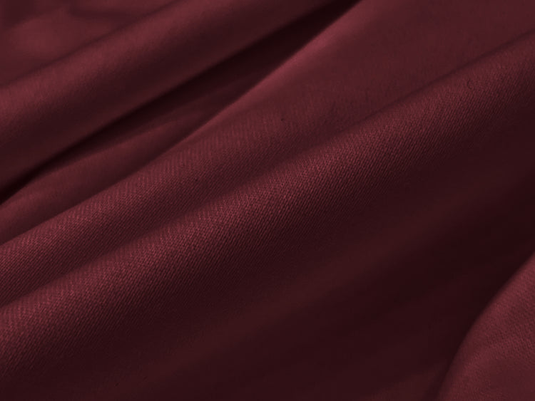 Smooth maroon fabric draped in elegant folds, creating a soft and luxurious texture.