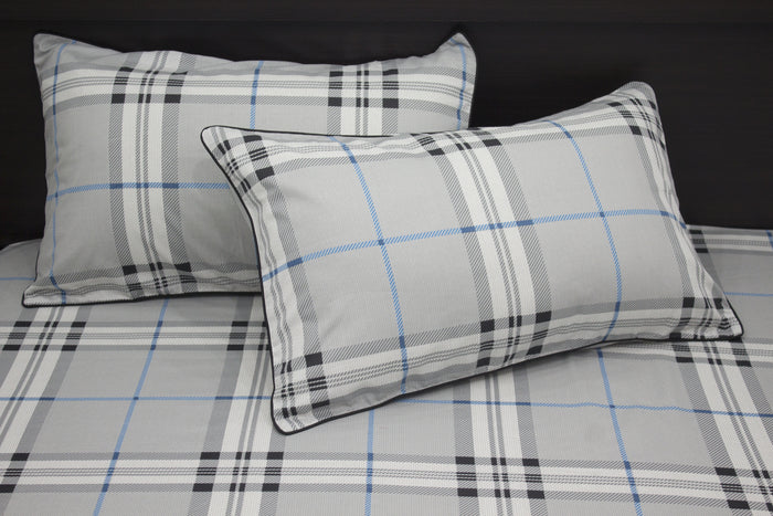 Two square pillows with a geometric pattern on a bed, primarily in gray, blue, and white colors.