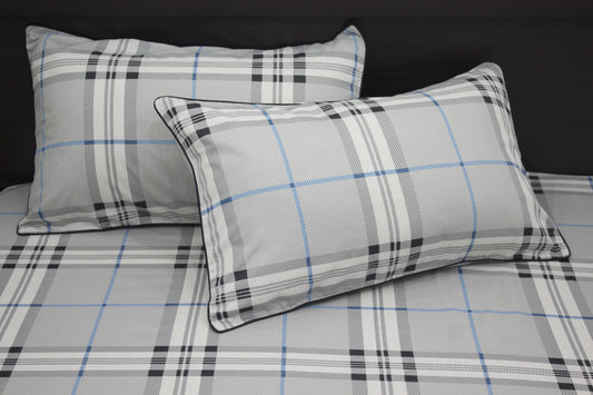 Two square pillows with a geometric pattern on a bed, primarily in gray, blue, and white colors.