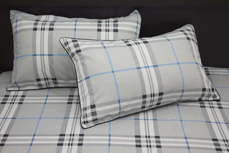 Two square pillows with a geometric pattern on a bed, primarily in gray, blue, and white colors.