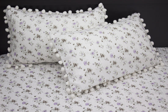 Two white pillows and bedsheet with a floral print and purple stripes on a bed.