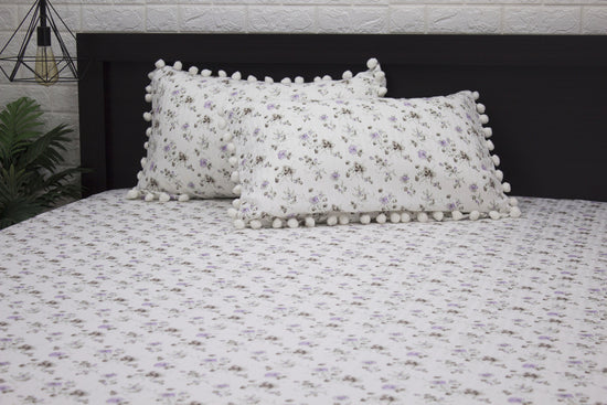 Two white pillows and bedsheet with a floral print and purple stripes on a bed 1.