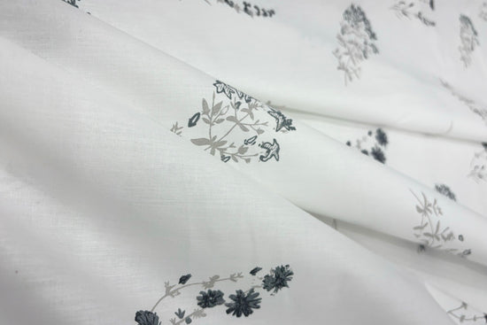 White fabric bedsheet with =floral patterns in grey and black.