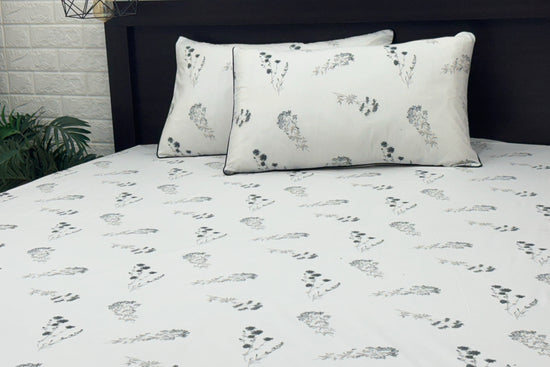 white bed sheets featuring a floral pattern. Two matching pillows .